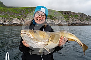 Happy young woman holding big arctic cod. Norway happy fishing. Fisherwoman with cod fish in hands