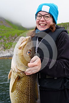 Happy young woman holding big arctic cod. Norway happy fishing. Fisherwoman with cod fish in hands