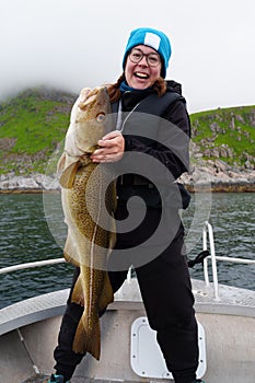 Happy young woman holding big arctic cod. Norway happy fishing. Fisherwoman with cod fish in hands