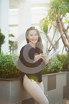 Happy young woman holding book fond of literature analyzing novel during leisure time on terrace of campus cafe in sunny day