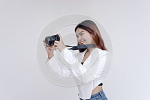 A happy young woman holding a camera in eye-level while taking pictures. Isolated on a white background