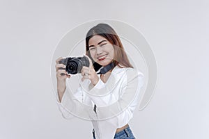 A happy young woman holding a camera in eye-level while taking pictures. Isolated on a white background