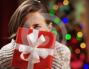 Happy young woman holding christmas present box in front of face