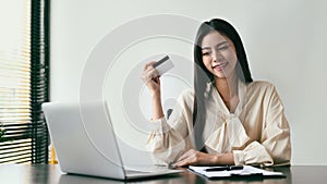 Happy young woman holding credit card and using laptop for making payment online. Online shopping, e-commerce concept