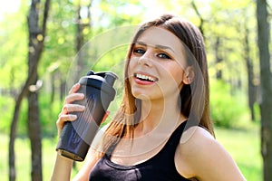 Happy young woman holding a glass of water in a summer park