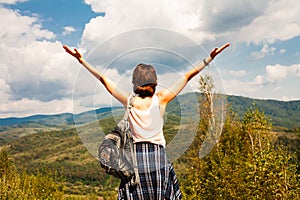 Happy young woman holding her hands up and enjoying beautiful mountain landscape. Back view. Freedom concept. Vacation in the