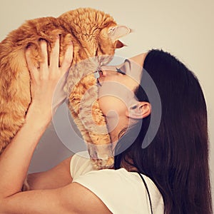 Happy young woman holding and hugging with love on the hands her red maine coon kitten and kissing. Closeup
