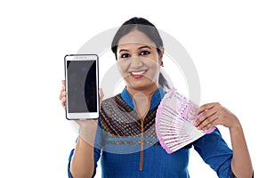 Happy young woman holding Indian currency and mobile phone