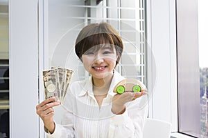 Happy young woman holding Japanese Yen and toy car