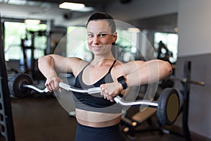 Happy young woman holding olympic bar in gym