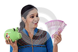 Happy young woman holding a piggy bank and Indian rupee notes