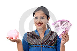 Happy young woman holding a piggy bank and Indian rupee notes