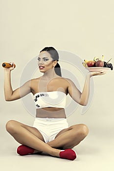 Happy young woman holding a plate with fruits in one hand and du