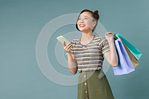 Happy young woman holding shopping bags and mobile phone over light blue background