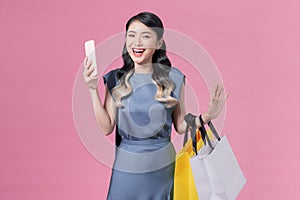 happy young woman holding shopping bags and mobile phone over pink background