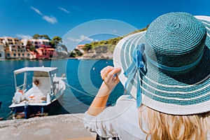 Happy young woman holding straw hat enjoying vacations in Assos village in front of emerald bay of Mediterranean sea