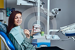 Happy young woman holding a toothbrush and denture in a dentist office.