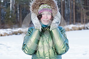 Happy young woman holding woolly mittens near her head in winter forest outdoors