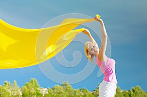 Happy young woman holding yellow scarf in the wind