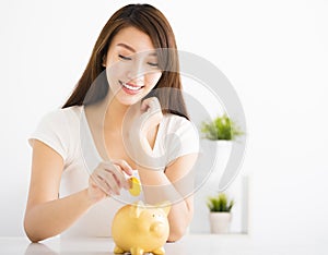 Happy young woman Inserting Coin In Piggy bank