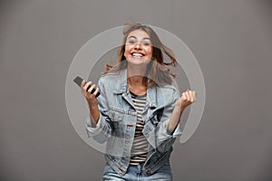 Happy young woman in jeans jacket clenching her fists in winner