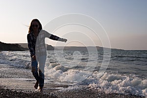 Happy young woman in jeans runs along the water by the ocean.