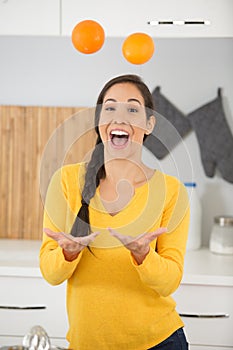 happy young woman joggling with oranges in kitchen