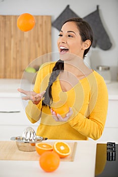 happy young woman joggling with oranges in kitchen