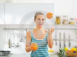 Happy young woman joggling with oranges in kitchen
