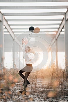 Happy young woman jumping with balloons in sunlight