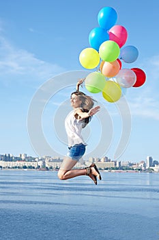 Happy young woman jumping with colorful balloons