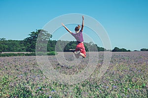 Happy young woman jumping in field of purple flowers