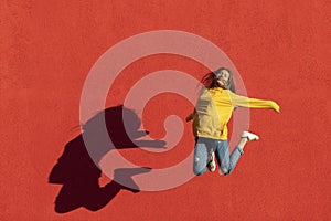 Happy young woman jumping midair in front of red wall.
