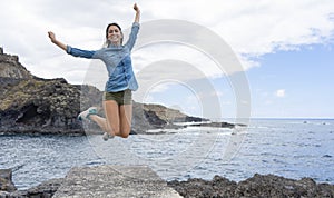 Happy young woman jumping in from of the sea with casual clothes, celebrating freedom and successful. Teenager excitement jump