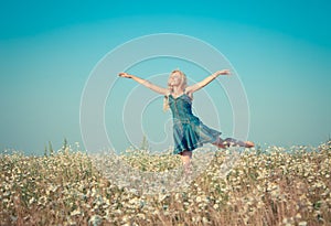 The happy young woman jumps in the field of camomiles