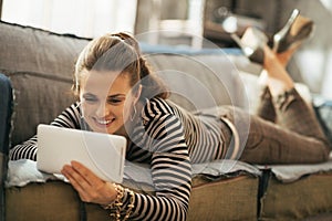 Happy young woman laying on couch and using tablet