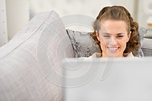 Happy young woman laying on divan with laptop