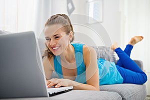 Happy young woman laying on divan and using laptop