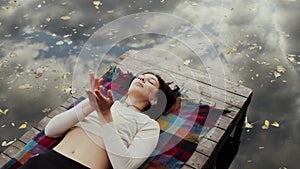 Happy young woman lays on pier and meditations by river at autumn day