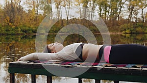 Happy young woman lays on pier and meditations by river at autumn day