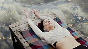 Happy young woman lays on pier and meditations by river at autumn day