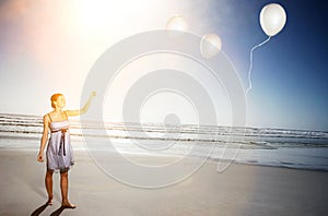 Happy young woman letting go of balloons on beach
