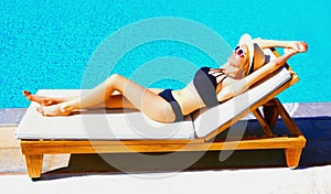 happy young woman lies relaxing on deckchair over blue water pool background