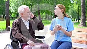 Happy young woman listening to music with old disabled man, supporting patient