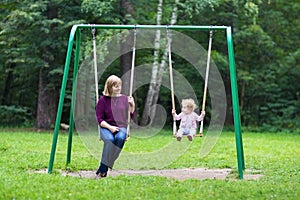 Happy young woman and a little baby girl swinging