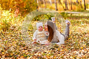 Happy young woman and little one-year-old girl lie on yellow leaves in autumn