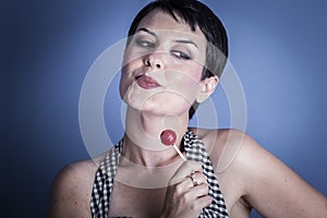 happy young woman with lollypop in her mouth on blue backg