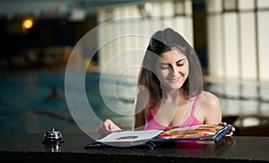 Happy young woman looking menu at swimming pool