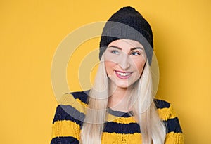 Happy young woman looking to side, model wearing woolen cap and sweater, isolated on yellow background. Pretty girl