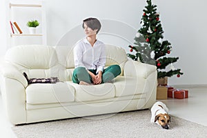 Happy young woman with lovely dog in living room with christmas tree. Holidays concept